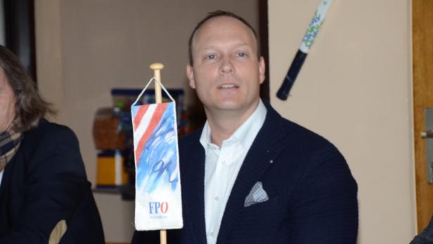 Ein Mann im Anzug steht neben einer kleinen FPÖ-Flagge.