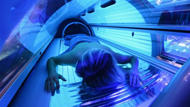 Eine Frau liegt in einem Solarium unter blauem Licht.