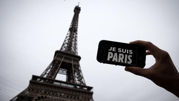 Eine Person hält ein Smartphone mit der Aufschrift „Je suis Paris“ vor dem Eiffelturm.