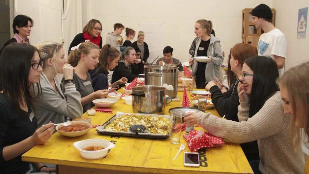Eine Gruppe junger Leute sitzt an einem langen, gelben Tisch und isst gemeinsam zu Mittag.