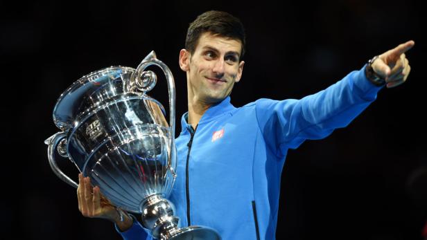 Novak Đoković hält eine Trophäe und zeigt mit dem Finger nach rechts.
