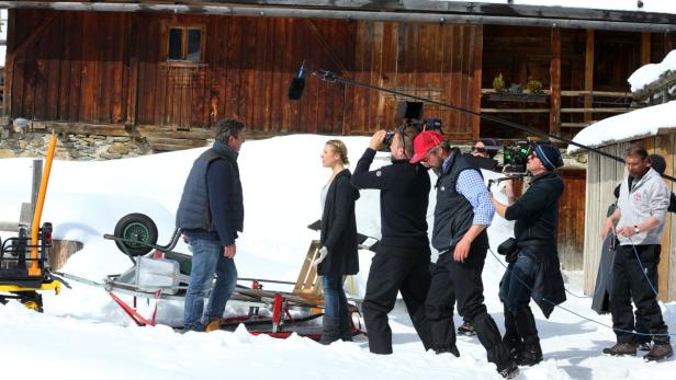 Ein Filmteam dreht eine Szene im Schnee vor einem Holzhaus.