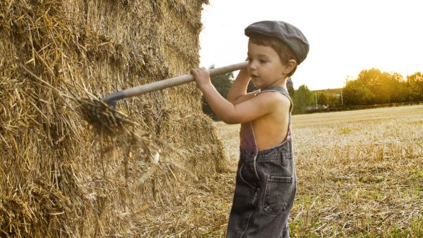 Ein Junge mit Mütze hantiert mit einer Heugabel an einem Heuballen.