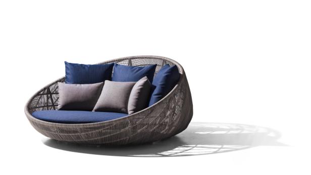 Ein graues, rundes Outdoor-Sofa mit blauen und grauen Kissen steht auf einem weißen Hintergrund.