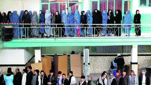 Frauen in Burkas und Männer stehen in einem Wahllokal in Afghanistan Schlange.