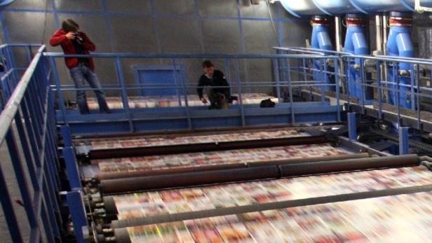 Zwei Personen beobachten eine große Druckmaschine in einer Fabrik.