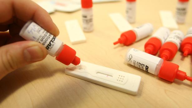 Eine Hand tropft Flüssigkeit aus einer Flasche auf einen Schwangerschaftstest.