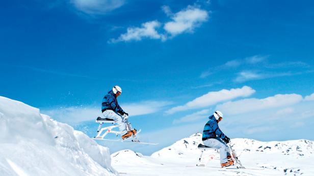 Zwei Personen fahren mit Skibikes auf einer schneebedeckten Piste.
