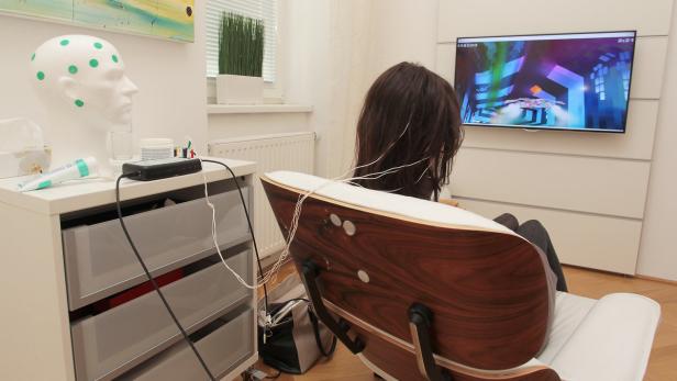 Neurofeedback: Elektroden sind am Kopf platziert, ein Computerspiel läuft automatisiert am Bildschirm, Musik im Hintergrund..