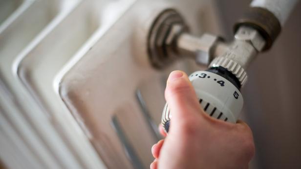 Eine Hand dreht an einem Heizkörperthermostat.