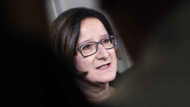 Eine Frau mit Brille spricht mit jemandem im Vordergrund.