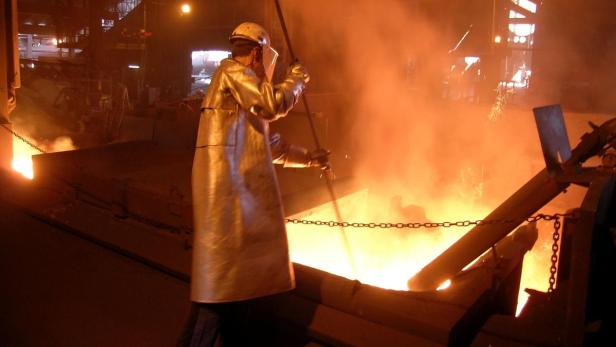 Ein Arbeiter in Schutzkleidung hantiert mit einem Werkzeug in der Nähe von flüssigem Metall.