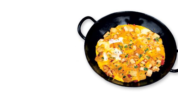 Eine Omelett-Pfanne mit Kartoffelwürfeln und Kräutern garniert.