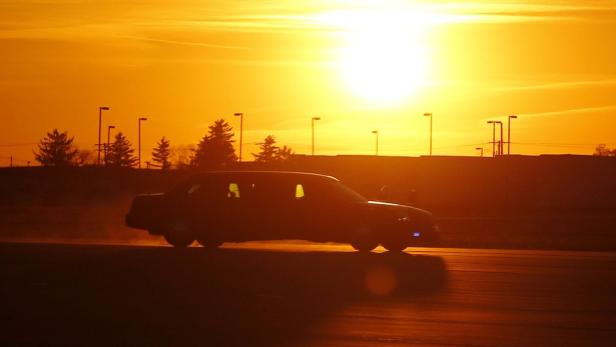 Eine dunkle Limousine fährt in der Abenddämmerung auf einer Straße.