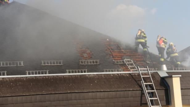 Feuerwehrleute bekämpfen einen Brand auf einem beschädigten Dach.