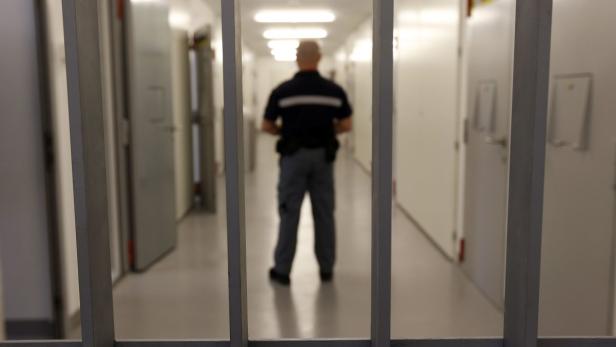 Ein Justizvollzugsbeamter steht in einem Gefängnisflur hinter Gittern.