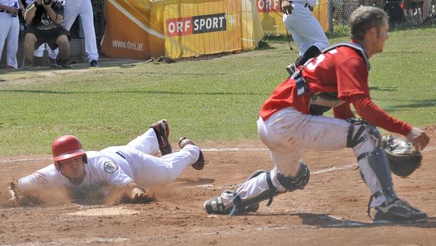 Ein Baseballspieler gleitet in die Homebase, während der Fänger auf ihn wartet.