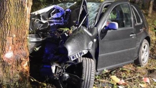 Ein schwarzes Auto ist gegen einen Baum gefahren und stark beschädigt.