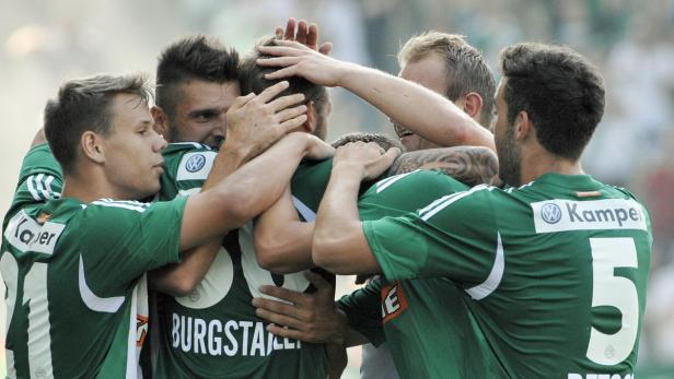Mehrere Fußballspieler in grünen Trikots umarmen sich auf dem Spielfeld.