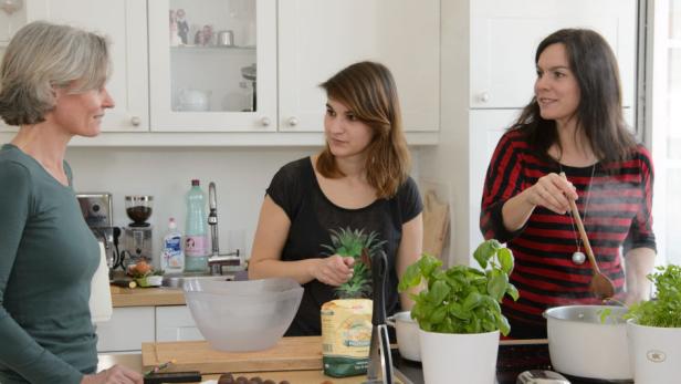 Drei Frauen stehen in einer Küche und bereiten Essen zu.