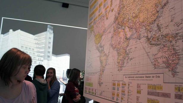 Eine Gruppe von Menschen betrachtet eine große Weltkarte in einer Ausstellung.