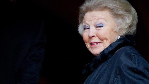 Königin Beatrix lächelt in einem dunklen Mantel mit Pelzkragen.