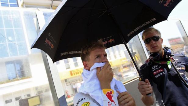 Sebastian Vettel wird von einem Mitarbeiter mit einem Handtuch und einem Regenschirm versorgt.