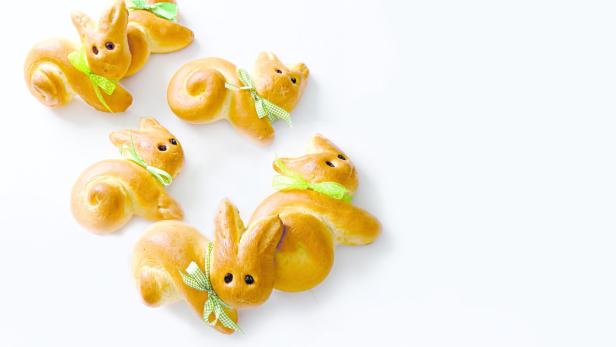 Mehrere süße Osterhasen aus Hefeteig mit Schleifen auf einem weißen Hintergrund.