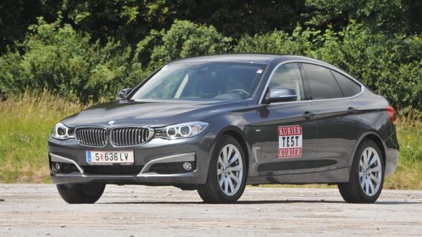 Ein grauer BMW steht auf einer Betonfläche vor grünen Büschen.