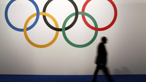 Eine Person geht an den Olympischen Ringen an einer Wand vorbei.