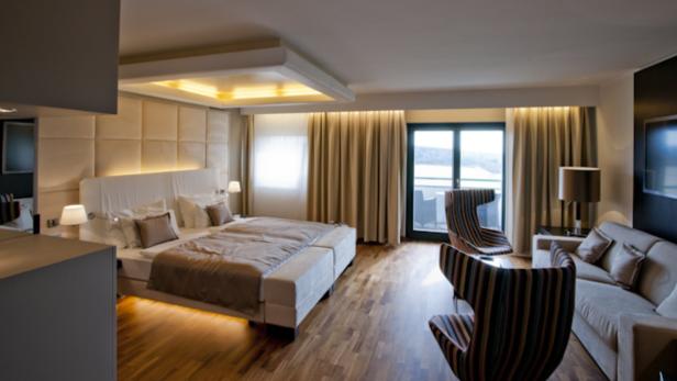 Ein helles Hotelzimmer mit Doppelbett, Sofa und Balkon mit Seeblick.