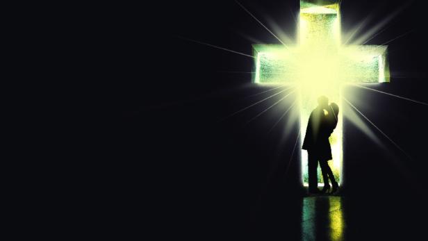 Ein Paar küsst sich vor einem hell erleuchteten Kreuz.