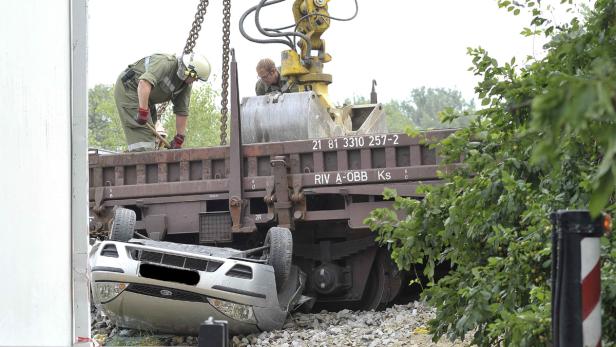 Ein Auto liegt unter einem Güterwagen, während Arbeiter die Situation begutachten.