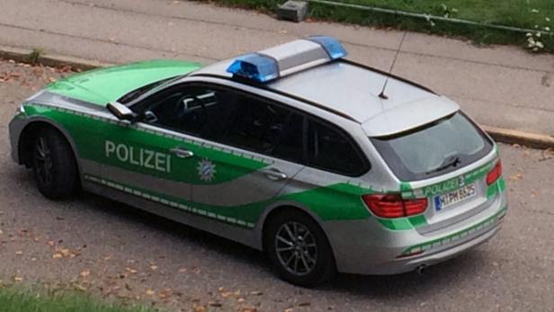 Ein silberner Kombi der bayerischen Polizei mit Blaulicht auf dem Dach steht auf der Straße.