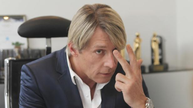 Ein Mann im Anzug gestikuliert mit seiner Hand vor dem Gesicht.