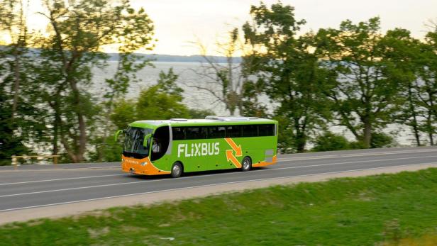 Ein grüner Flixbus fährt auf einer Straße entlang eines Sees.