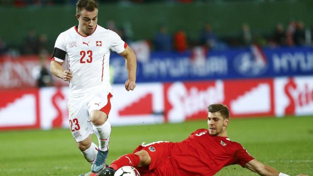Ein Fußballspieler der Schweiz läuft mit dem Ball, während ein österreichischer Spieler am Boden liegt.