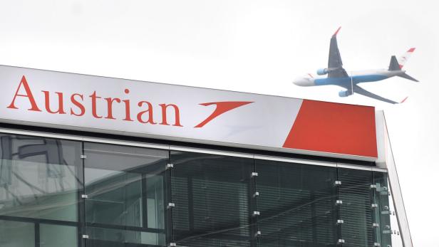Ein Flugzeug der Austrian Airlines überfliegt ein Gebäude mit dem Logo der Fluggesellschaft.