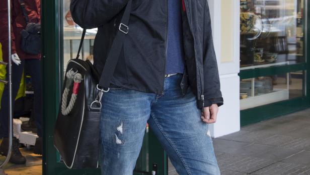 Eine Frau mit Jacke und Umhängetasche steht vor einem Geschäft.