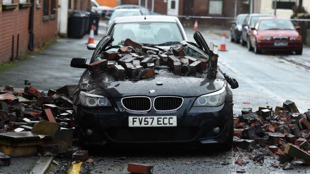Ein schwarzer BMW ist mit Ziegelsteinen bedeckt und beschädigt.