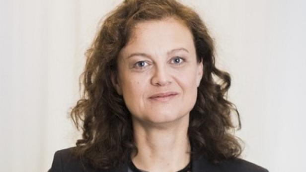 Porträt einer Frau mit braunen, lockigen Haaren und einem dunklen Blazer.