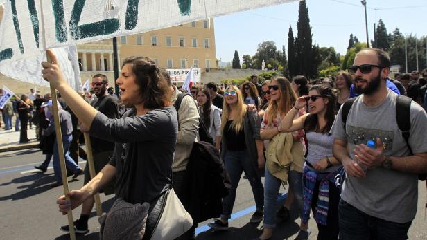 Eine Menschenmenge demonstriert mit einem Transparent in einer städtischen Umgebung.