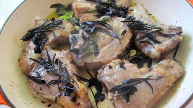 Lammkoteletts werden in einer Pfanne mit Rosmarin und Salbei gebraten.