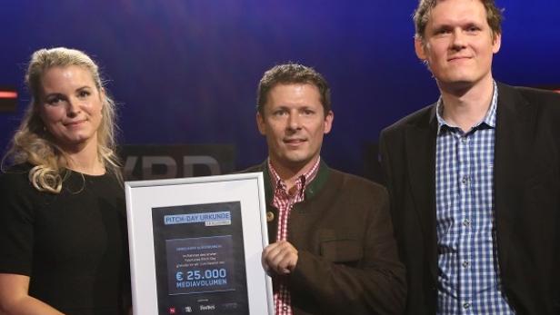 Drei Personen präsentieren eine „Pitch-Day“-Urkunde über 25.000 Euro Medienvolumen.