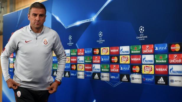 Ein Mann im Galatasaray-Trainingsanzug steht vor einer Wand mit Champions-League-Logos und Sponsorenlogos.