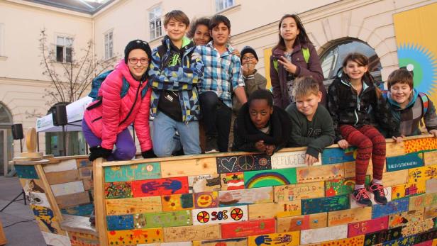 Eine Gruppe von Kindern steht und sitzt auf einem bemalten Holzboot.