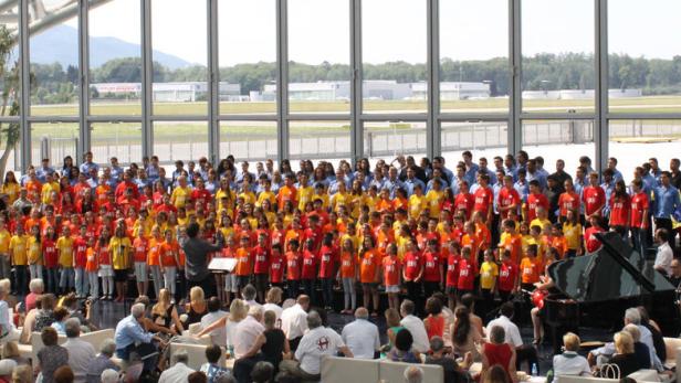 Ein großer Chor singt vor Publikum in einem hellen, modernen Gebäude.