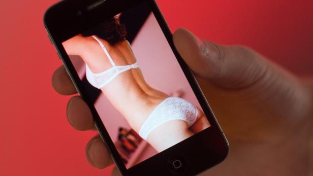 Eine Hand hält ein Smartphone, auf dessen Bildschirm eine Frau in Unterwäsche zu sehen ist.