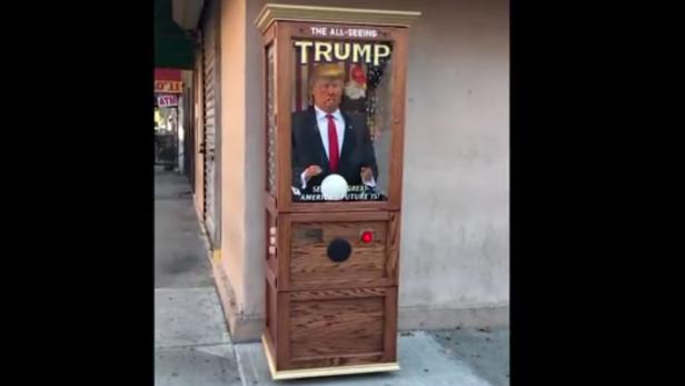 Ein Wahrsagerautomat mit einer Figur von Donald Trump steht auf einem Bürgersteig.