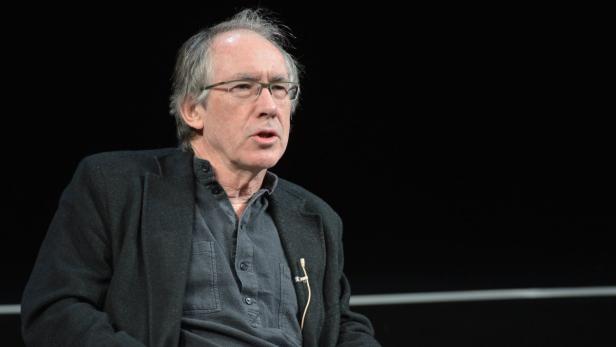 Ein Mann mit Brille und dunkler Jacke spricht vor einem dunklen Hintergrund.